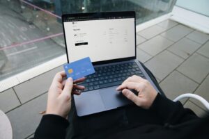 Laptop mit Einkaufs-Seite und davor eine Hand die eine Bank-Karte hält