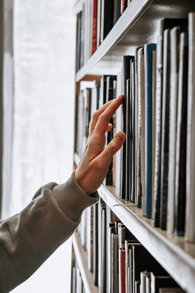 Hand, die über Buchrücken in einem Regal fährt